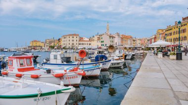 Rovinj Hırvatistan 27 Ağustos 2024 Vibrant balıkçı tekneleri, açık mavi gökyüzü altındaki tuhaf pastel binaları yansıtarak Rovinjs limanının sakin sularında usulca yüzüyor.