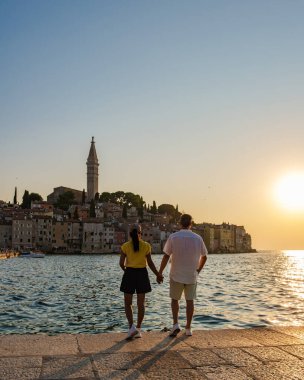 Güneş, Rovinj 'in pitoresk kasabasında el ele tutuşarak huzurlu bir anın tadını çıkarıyor. Işıldayan sular alacakaranlığın ılık tonlarını yansıtıyor ve sakin bir atmosfer yaratıyor..