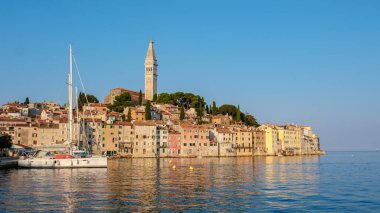 Güneş Rovinj 'in üzerinde batarken, gökyüzü sıcak renklerle boyanır ve güzel bir rıhtıma altın bir parıltı saçar. Limanda huzurlu yelkenlilerle kıyı boyunca uzanan renkli binalar..