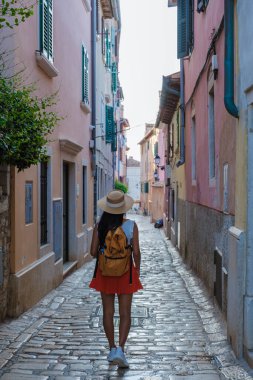 Bir gezgin, renkli binalar ve yeşilliklerle çevrili Rovinj 'in dar, kaldırımlı yollarında yürüyor. Sıcak öğleden sonra güneşi serüveninin tadını çıkarırken huzurlu bir atmosfer yaratıyor..