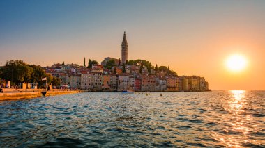 Güneş Rovinj 'in üzerinde batarken, canlı binalar rıhtım boyunca uzanır, renkleri sakin suyu aydınlatır. Alacakaranlığın ılık parıltısı bu sahil taşında büyülü bir atmosfer yaratıyor..