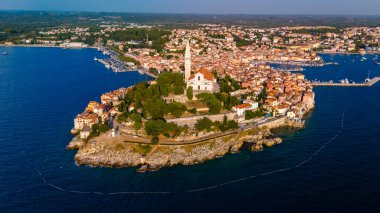 Rovinj Hırvatistan, sıcak bir günbatımı parıltısı altında büyüleyici kıyı manzarası, canlı mimarisi ve tarihi cazibesiyle ziyaretçileri cezbediyor. Huzurlu sular Büyüleyici ufuk çizgisini yansıtıyor.