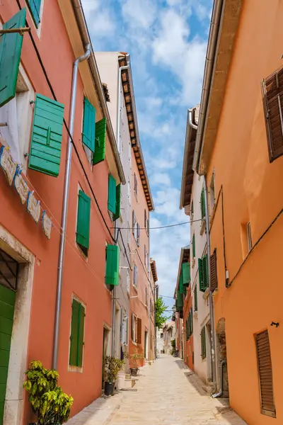 stock image One can wander through the historic streets of Rovinj, where vibrant orange and green buildings line the narrow pathway, bathed in warm sunlight under a soft blue sky filled with clouds.