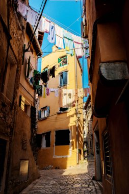 Clothes sway gently in the breeze above narrow cobblestone streets, bathed in golden sunlight. The charming buildings exude a warm glow, creating an inviting atmosphere in Rovinj. clipart