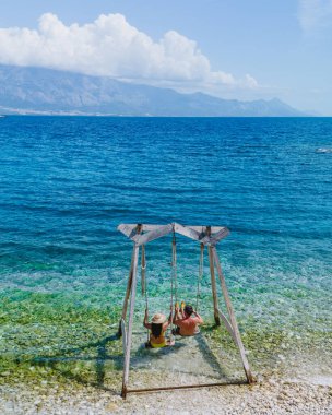 Hırvatistan 'ın Brac Adası' ndaki güzel bir sahilde, kristal berraklığında suyun güneşin altında parladığı ahşap bir salıncakta rahatlayan iki arkadaş mükemmel bir yaz kaçışı yaratıyor..