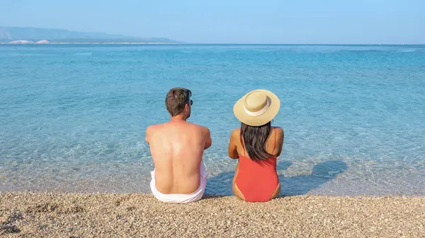 stock image A couple enjoys a tranquil afternoon on Brac Island, gazing across the clear turquoise waters. The warm sun casts a glow, a diverse couple of man and woman at Zlatni Rat Beach