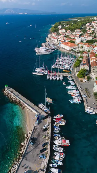 stock image An enchanting harbor on Brac Island showcases numerous boats anchored peacefully while crystal-clear waters meet the sandy beach. Colorful houses and lush greenery create a picturesque coastal escape.