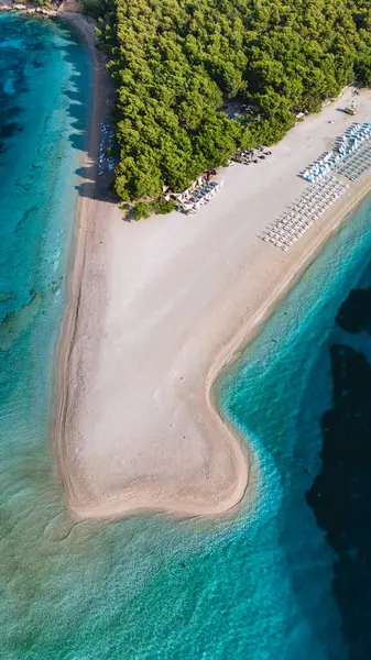 Brac Adası 'ndaki kıyı şeridi, canlı yeşilliklerle çevrili turkuaz sulara uzanan yumuşak kumları ortaya çıkarıyor. Güneş pansiyonları kumsalı dolduruyor, güneşin altında rahatlamaya davet ediyor. Zlatni Rat Sahili Hırvatistan