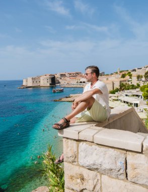 Bir gezgin, berrak turkuaz denizin ve Dubrovnik 'in tarihi mimarisinin nefes kesici manzarasının tadını çıkarıyor. Güneş ışıl ışıl parlıyor, rahatlama ve keşif için mükemmel bir atmosfer yaratıyor..