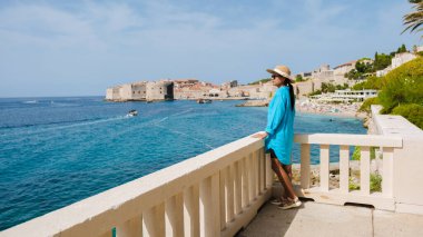 Canlı, mavi örtülü bir kadın, Dubrovnik Hırvatistan 'ın tarihi kıyı şeridinin nefes kesen manzarasının keyfini çıkarıyor. Ilık güneşlerde yüzen teknelerin ışıl ışıl denizde süzülmesini seyrediyor..