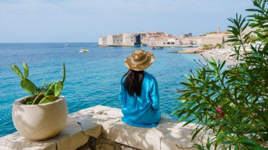Deniz kenarında oturan bir gezgin, güzel antik Dubrovnik kenti Hırvatistan 'a bakıyor. Işıl ışıl turkuaz sular güneşi yansıtırken, tekneler de tarihi duvarların etrafında yavaşça sürükleniyor..