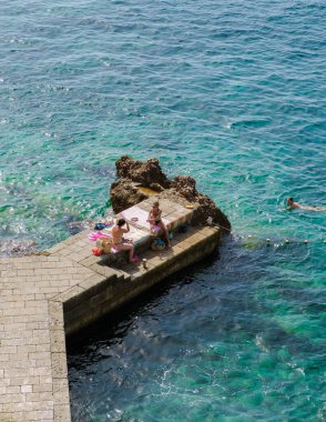 Dubrovnik Hırvatistan 9 Eylül 2024, Dubrovnik 'teki kayalık bir rıhtımda, kristal berrak sular ve yumuşak dalgaların sesleriyle çevrili güneşli bir günün tadını çıkarıyor. 