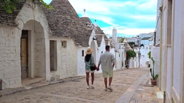Bir çift, Alberobello, Puglia 'nın büyüleyici caddelerinde romantik bir gezinti yapıyor. Bu bölgenin manzarasını belirleyen ikonik trulli evlerle çevrili.