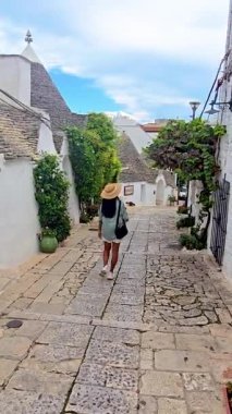 İtalya 'nın Puglia şehrinde yer alan Alberobello' nun görkemli ve büyüleyici sokaklarında sakin bir yürüyüş yapan bir kadın, yemyeşil çimenliklerle çevrili ikonik trulli mimarisini gözler önüne seriyor.