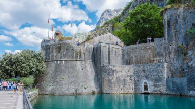 24 Eylül 2024 'te Kotor Montenegro' da ziyaretçiler, sakin turkuaz suların üzerinde görkemli bir şekilde yükselen Kotor kalesine hayran kalarak liman boyunca geziniyorlar.