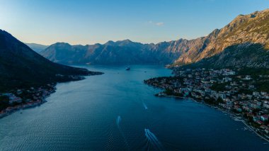 Nefes kesici Kotor Körfezi, çarpıcı dağlarla çevrili günbatımının yumuşak parıltısıyla aydınlanır. Tekneler sakin sularda zarifçe süzülüyor, sakin ve resimsel bir manzara yaratıyor..