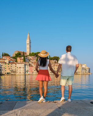 Hırvatistan 'ın Rovinj kentinin parıldayan sularında güneşli bir günde el ele tutuşan bir çift. Yüksek binalar ve bir kilise kulesi o an için pitoresk bir zemin yaratır..