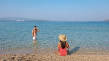 Öğleden sonra güneşli bir Brac Adası plajında bir kişi serin ve berrak suların tadını çıkarırken bir diğeri sıcak kumda dinleniyor ve yaz mutluluğunun ve huzurunun özünü somutlaştırıyor. Zlatni Rat Sahili