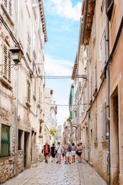 Rovinj Hırvatistan 27 Ağustos 2024 Ziyaretçiler, sıcak güneşin tadını çıkararak tarihi binalar ve canlı renklerle kaplı pitoresk bir kaldırım taşı caddesinde dolaşıyorlar. 