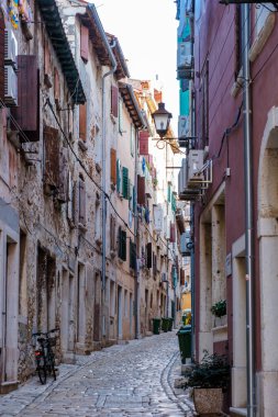 Rovinj 'deki tuhaf bir ara sokakta renkli panjurlarla süslenmiş yıpranmış taş duvarlar ortaya çıkıyor. Sabahın erken saatlerinde, bir bisikletin bir binaya dayandığı dar sokakta sıcak bir parıltı salıyor..