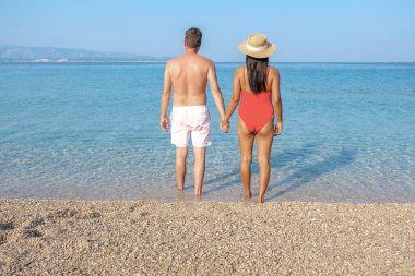 Brac Adası 'nın berrak suları boyunca el ele yürüyüp güneşin tadını çıkarıyorlar. Ayak sesleri yumuşak çakıl taşlarında yumuşak izler bırakır, romantik bir an yaratır..