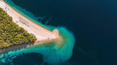 Altın kum, Brac Adası 'nın pırıl pırıl turkuaz sularını kuşatarak gezginleri güneşin tadını çıkarmaya davet eder. Yeşillik sahili kaplıyor, Zlatni Rat Sahili Hırvatistan