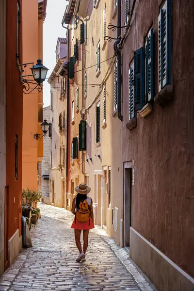 Rovinj 'in dar kaldırım taşlı sokaklarında gezinen bir gezgin, bu sıcak güneş ışığı ve bu kıyı taşının Akdeniz cazibesine batmış canlı renklerin ve tarihi mimarinin tadını çıkarıyor..