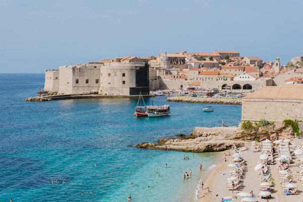 Волны мягко опускаются на песчаный берег Дубровника Хорватия, когда посетители наслаждаются теплым солнцем и чистой водой