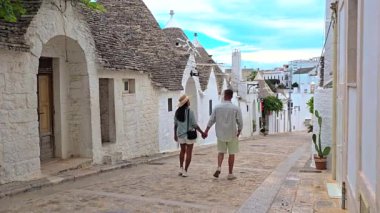 İtalya 'da Puglia' nın manzarasını tanımlayan ikonik Trulli binalarla çevrili Alberobello 'nun tuhaf ve büyüleyici sokaklarında el ele gezen hoş bir çift.