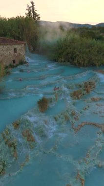 Gün batımının altın rengi altında, kristal berraklığında suların doğal kaya oluşumları üzerinde yavaşça aktığı Satürn Tuscany İtalya HidroTermal Hamamı 'nın altında büyüleyici bir termal yay keşfedin.