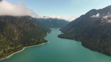Bir dağ gölünün kristal berrak suları yükselen zirveleri ve canlı yeşillikleri yansıtırken sakin bir manzara. Doğanın huzuru bu büyüleyici ortamda ortaya çıkar. Plansee Avusturya