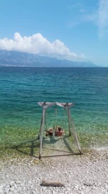 Kırsal bir salıncakta yavaşça sallanan iki arkadaş, berrak turkuaz suları ve çarpıcı dağ manzaralarıyla plajın sakin atmosferinin tadını çıkarıyorlar. Brac Adası Hırvatistan