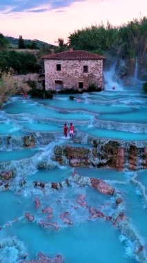 Bir çift maceracı nefes kesici turkuaz termal sularda geziniyor. Etrafı manzaralı kırsallarla çevrili. Saturnia Toskana İtalya Hidroelektrik Hamamı