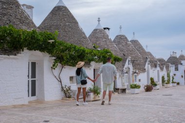 Alberobello Puglia İtalya 'nın görkemli caddelerinde, alacakaranlık, alacakaranlıkta bembeyaz binalara hafif bir parıltı saçarken ikonik trulli evlerle çevrili bir çift el ele dolaşır..
