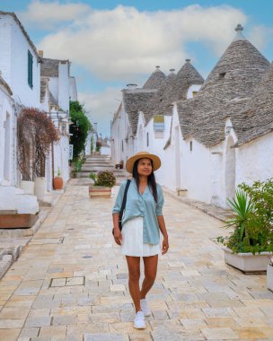 Wandering through the picturesque streets of Alberobello Puglia Italy, a traveler enjoys the unique trulli architecture under a cloudy sky. clipart