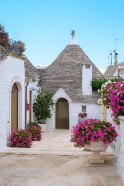 Resimli trulli evlerde dolambaçlı yollar, eşsiz taş çatıları, canlı renklerde açan çiçeklerle güçlendirilmiş. Güneş ışığı Alberobello Puglia 'nın bu cennet gibi batışına sıcacık bir ışık saçıyor..