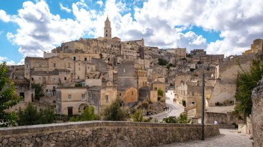 Matera İtalya 'nın tarihi sokaklarında dolanan ziyaretçiler, antik taş konutlara ve ikonik çan kulesine hayret ediyorlar. Dramatik bulutlar bu eşsiz İtalyan manzarasının güzelliğini arttırır..