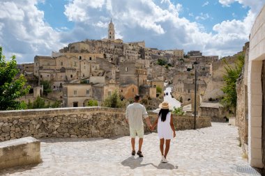 İki aşık, Matera İtalya 'nın tarihi cazibesiyle çevrili kaldırım taşı patikalarında el ele dolaşıyorlar. Parlak, bulutlarla dolu gökyüzüne karşı büyüleyici bir mimari..