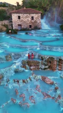 Turkuaz turkuaz kaplıcaları keşfedin. Ziyaretçiler rahatlarken ve doğal güzelliğin tadını çıkarırken yemyeşil çevrelerde yuva yapmış durumdalar. Saturnia Toskana İtalya Hidroelektrik Hamamı