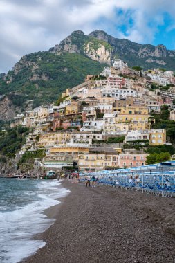 Positano, Amalfi Sahili 'nde, ziyaretçiler çakıllı sahil boyunca ayaklarında hafif dalgalarla gezerken kayalıklarda renkli binalar barındırıyor..