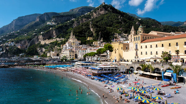 Visitors bask in the sun along the vibrant Amalfi Coast, surrounded by stunning cliffs, colorful umbrellas, and glistening waters. A perfect day for relaxation and enjoying the coastal beauty.