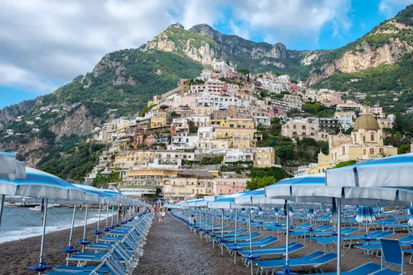 Positano 'nun güneşli kıyılarında ziyaretçiler güneşlenirken tepenin aşağısına renkli binalar dökülüyor. Burada ikonik plaj şemsiyeleri muhteşem uçurumların altındaki manzarayı işaretliyor.. 