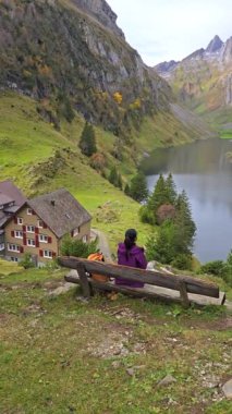 İsviçre Alpleri 'ne yerleşmiş bir insan göle bakan bir bankta dinleniyor. Etrafı görkemli dağlar ve sonbahar yapraklarıyla çevrili. Falensee Gölü Alp Dağları, Appenzell Innerrhoden, İsviçre.