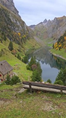 İsviçre Alpleri 'ne yerleşmiş, sonbahar yapraklarını yansıtan sakin bir göle bakan tuhaf bir ev. Yüksek dağlarla çevrili Falensee Gölü Alpleri, Appenzell Innerrhoden, İsviçre.