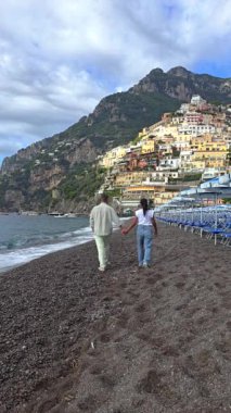 Positano 'nun pitoresk kıyı şeridi boyunca yürüyen bir çift olarak huzurlu bir anın tadını çıkarın. Arkaplanda renkli kayalıklar ve canlı evler var. İtalya 'da sonbahar güzel bir manzara resmediyor.