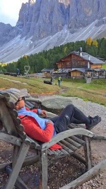 Dolomitlerde dingin bir öğleden sonra, bir kadın kırsal bir sandalyede uzanmış, dağların huzurlu güzelliğinin tadını çıkarırken. Geisler Alm Odle Dağı, Alto Adige, Dolomitler, İtalya