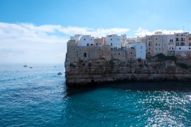 Polignano ve Mare Italya, parlak İtalyan güneşinin altında, Puglia 'nın engebeli kayalıklarına tutunan, mavi sulara tepeden bakan ve dalgalarda sallanan tekneleri nazikçe davet eden binalar..