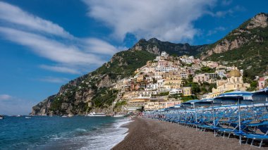Dalgalar rengarenk uçurum kenarındaki güneşte güneşlenen evlerle çerçevelenmiş çakıl taşlı kıyılara nazikçe çarpar. Şemsiyeler sahilde, Positano İtalya 'da Amalfi Sahili' nde.