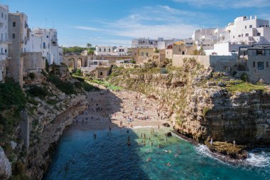 Puglia 'daki Polignano a Mare, ziyaretçiler baş döndürücü uçurumlar ve beyaz binalarla sakin bir koyda toplanıyor, deniz kenarındaki güneşli günlerin tadını çıkarıyor ve canlı kıyı manzarasını keşfediyorlar. İtalya