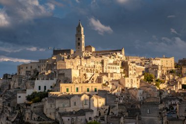 Ortaçağ mimarisinin arkasında güneş batarken altın ışık Matera 'nın tarihi mağara evlerini yıkıyor. Bu büyüleyici manzara, bu eşsiz İtalyan kasabasının özünü yansıtıyor..